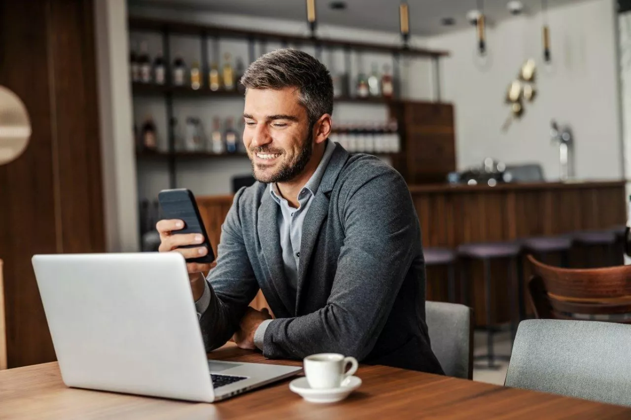 &lt;p&gt;A happy businessman is sitting in a coffee shop and checking on his bank account on the mobile. There is a laptop on a table. A man using the phone for e-banking&lt;/p&gt;