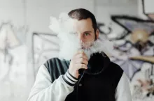 young man vaping his electronic cigarette in a suburb with graffiti in the background. Man blowing puffs of steam. Give up smoking. bad habits.