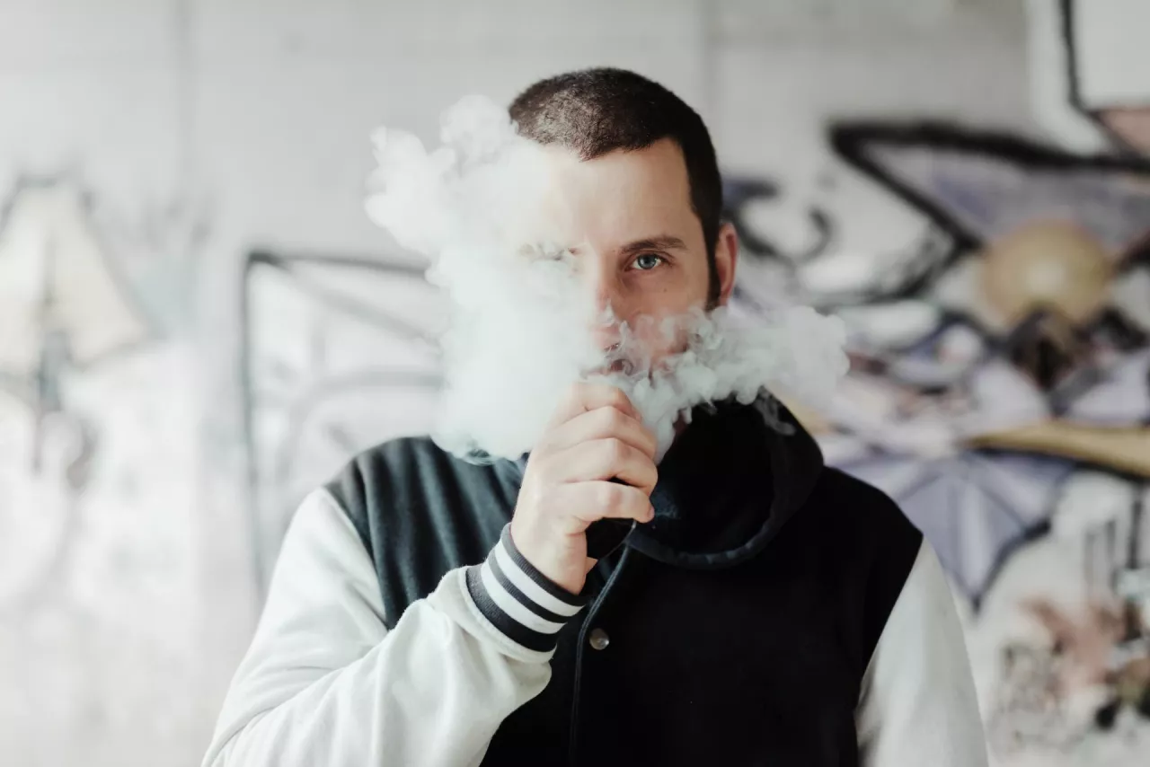 young man vaping his electronic cigarette in a suburb with graffiti in the background. Man blowing puffs of steam. Give up smoking. bad habits.