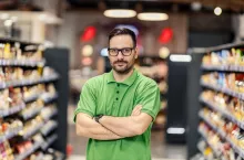 A professional salesman is standing with arms crossed at supermarket and looking at the camera.