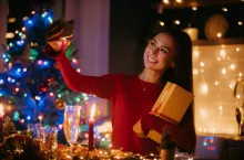 Smiling young woman holding gift box and making selfie while enjoying New Year Eve at home