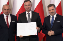 Prezydent Andrzej Duda prezentujący podpis pod ustawą o ograniczeniu handlu w niedziele, 2018 r. Obok niego Alfred Bujara i Piotr Duda z Solidarności (fot. YouTube)