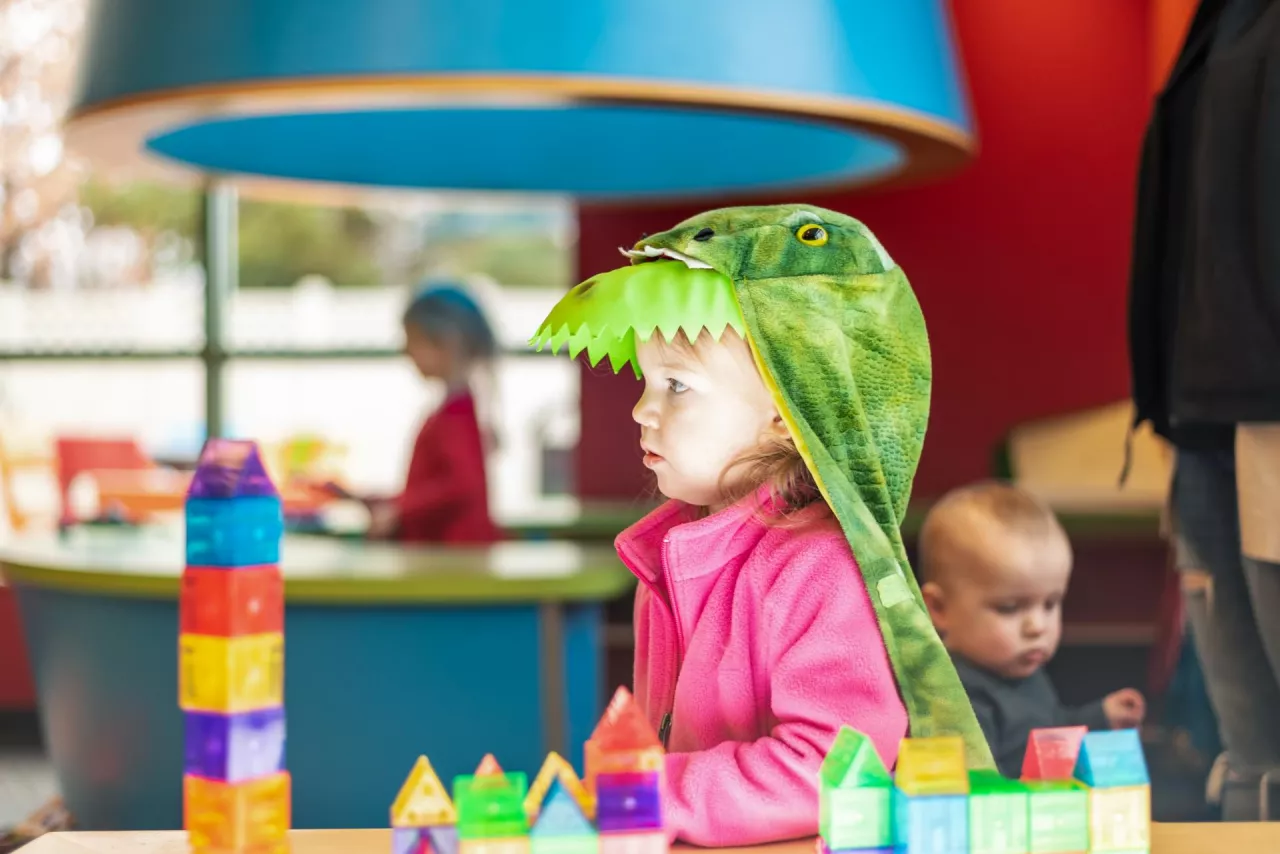 Toddler girl dressed in a dinosaur costume playing with toys - creative play