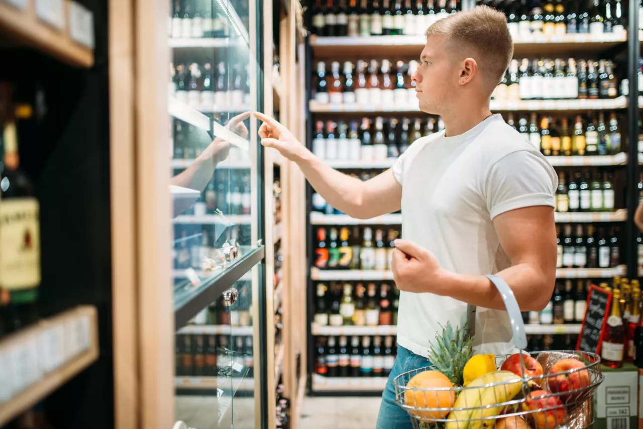 Male customer with basket choosing beer in supermarket. Shopping in food store, alcohol section on background