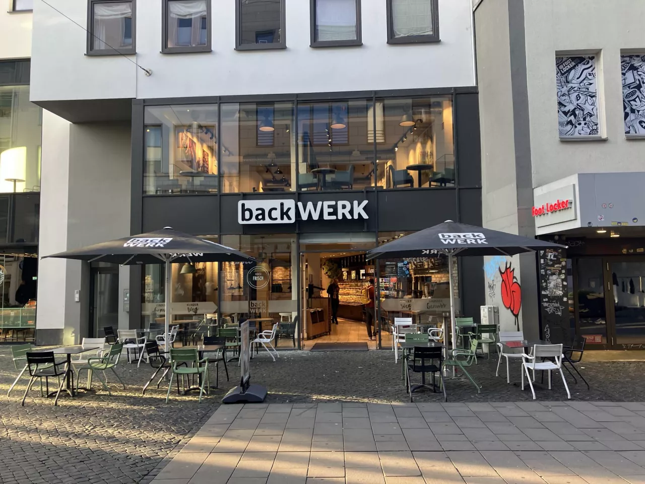 Sklep BackWerk w centrum miasta ilustruje swoją rolę łączącą piekarnię z punktem sprzedaży detalicznej, z miejscami siedzącymi w stylu kawiarnianym wewnątrz i na zewnątrz, w strefie dla pieszych. (fot. Sebastian Rennack)