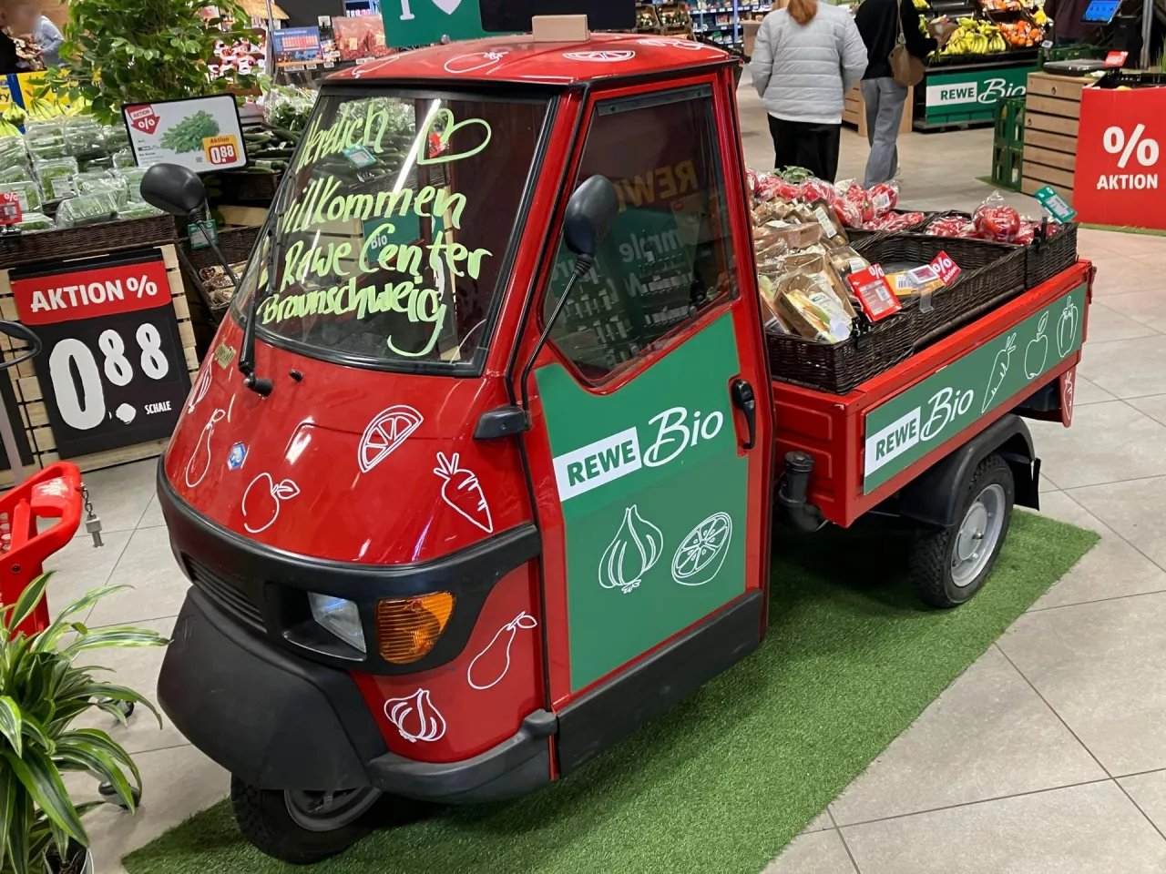 Klasyczny skuter Vespacar przy wejściu do sklepu Rewe sygnalizuje wieloletnie, lokalne zakorzenienie. Przedstawia sprzedawcę jako zaufanego sąsiada, a nie anonimowego operatora sieci. (Fot. Sebastian Rennack)